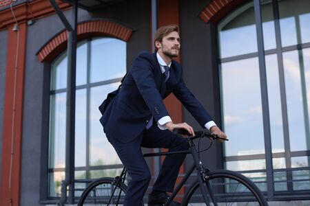 Handsome businessman riding bicycle to work on urban street in morning.の写真素材