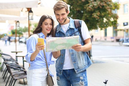 Beautiful young couple holding a map and smiling while standing outdoors.の写真素材