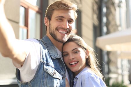 Beautiful young couple in summer clothes smiling and taking selfie photo together while walking...