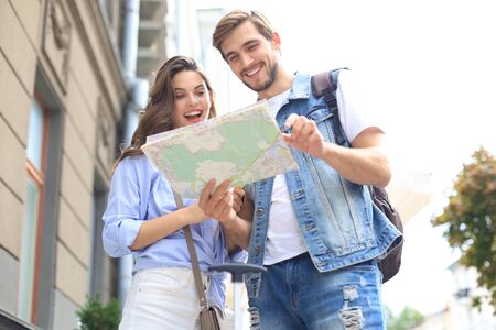 Beautiful young couple holding a map and smiling while standing outdoors.の写真素材