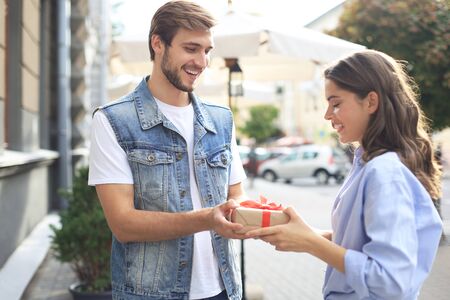 Astonished excited couple in summer clothes smiling and holding present box together while standing on city street.の写真素材