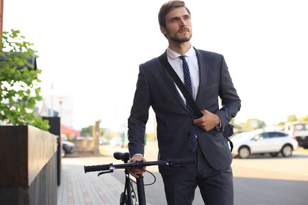Pensive young businessman walking with bicycle on the street in city.の写真素材