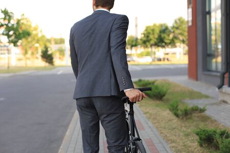 Cropped image of a young man in suit walking with a bicycle on a city street.の写真素材