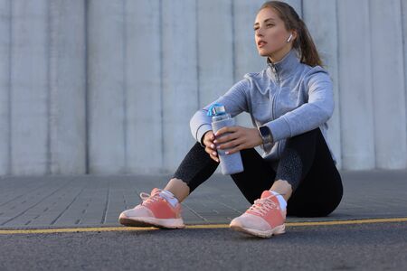 Beautiful young woman in sports clothing drinking water after sport exercise outdoors