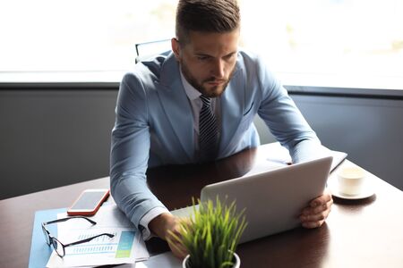 Good looking business man is holding laptop while sitting in the office