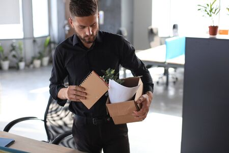 Sad dismissed worker is taking his office supplies with him from officeの写真素材
