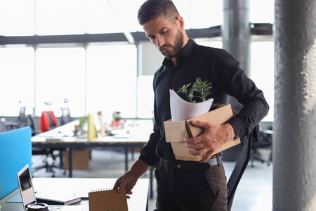 Sad dismissed worker is taking his office supplies with him from officeの写真素材