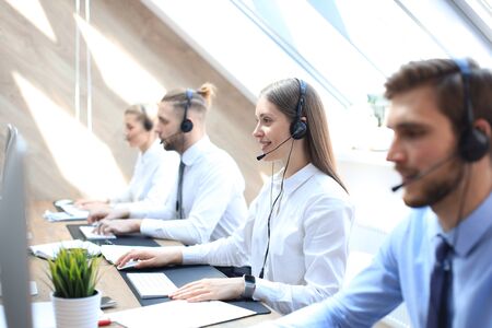 Female customer support operator with headset and smiling accompanied by her teamの写真素材