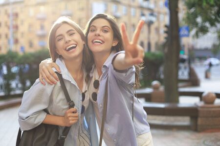 Two young smiling hipster women in summer clothes posing on street.Female showing positive face emotionsの写真素材