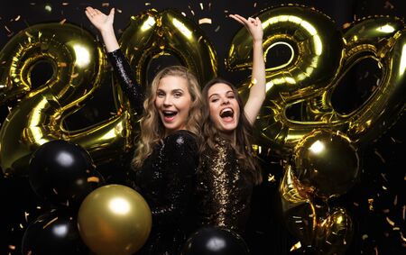 Happy gorgeous girls in stylish sexy party dresses holding gold 2020 balloons, having fun at New Year's Eve Partyの写真素材
