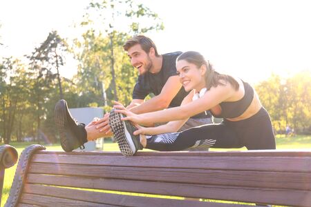 Happy young couple exercising together in a park, stretching exercises