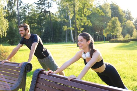 Smiling sports loving couple in park outdoors making sport exercises