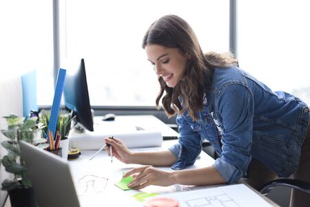 Young architect drawing with a compass on blueprint and smiling while working in the creative office