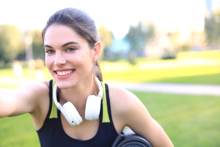Beautiful happy young sports woman holding fitness rug in urban park.の写真素材