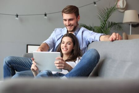 Young couple watching media content online in a tablet sitting on a sofa in the living room