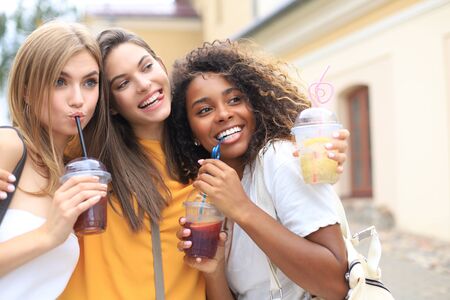 Three trendy cool hipster girls, friends drink cocktail in urban city backgroundの写真素材