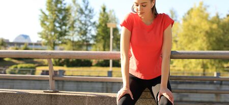 Young fitness attractive sporty girl resting after intensive evening run outdoor at sunset in city