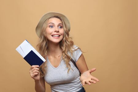 Beautiful blonde woman wearing summer clothes posing with passport with tickets over beige backgroundの写真素材