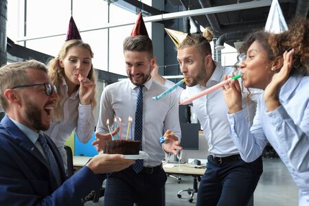 Happy business team with birthday cake are greeting colleague at office partyの写真素材