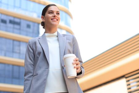 Portrait of successful business woman going to work with coffee walking near office building on city streetの写真素材