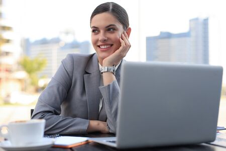 Portrait of successful business woman using laptop and smiling while sitting in cafe, outdoorの写真素材