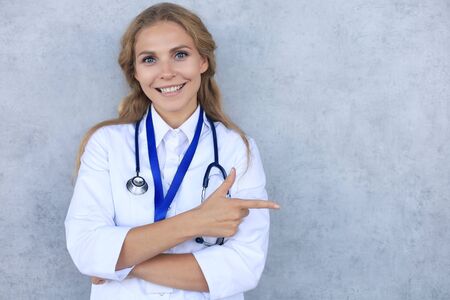 Happy smiling female doctor in white uniform coat and stethoscope, isolated over grey background.の写真素材