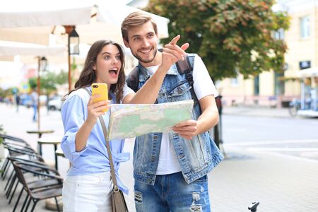 Beautiful young couple holding a map and smiling while standing outdoorsの写真素材