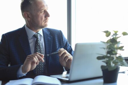Focused mature businessman deep in thought while sitting at a table in modern officeの写真素材