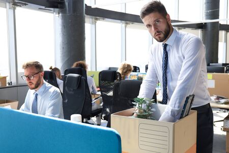 Sad dismissed worker are taking his office supplies with him from office.の写真素材