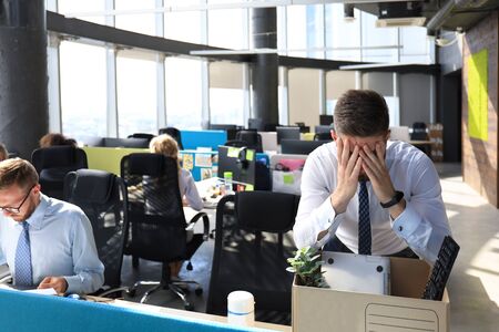 Sad dismissed worker are taking his office supplies with him from office.