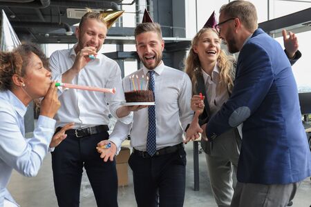 Happy business team with birthday cake are greeting colleague at office party.の写真素材