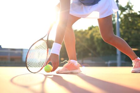 Tennis player raises a tennis ball from the clay court during the gameの写真素材
