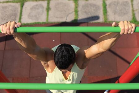 Muscular guy pulling up on horizontal bar outdoor.の写真素材