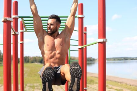 Strong man doing statics exercise on horizontal bar, having workout outdoors at sunny day.