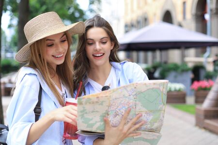 Holidays and tourism concept - beautiful girls looking for direction in the city