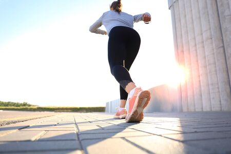 Rear view of young woman running outdoor at sunset or sunrise in cityの写真素材