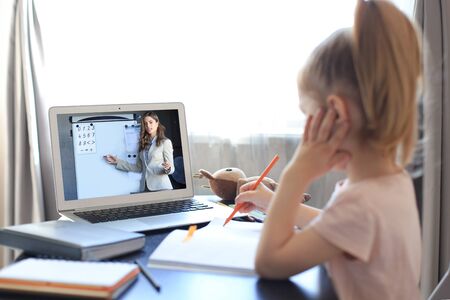 Distance learning. Cheerful little girl using laptop computer studying through online e-learning...