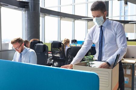 Dismissal employee in preventive medical mask in an epidemic coronavirus. Sad dismissed worker are taking his office supplies with him from officeの写真素材