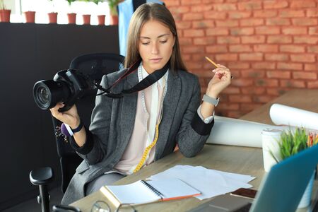 Beautiful young woman looking at her notes and holding digital camera while sitting in her workshopの写真素材