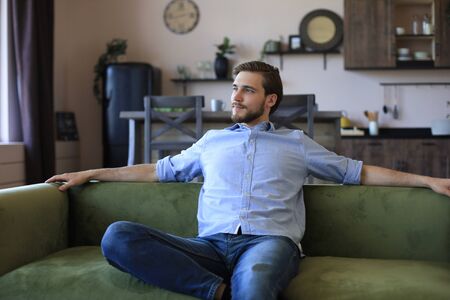 Handsome young business man is looking relaxed while sitting on the couch at homeの写真素材