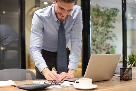 Young modern business man analyzing data using laptop while working in the officeの写真素材