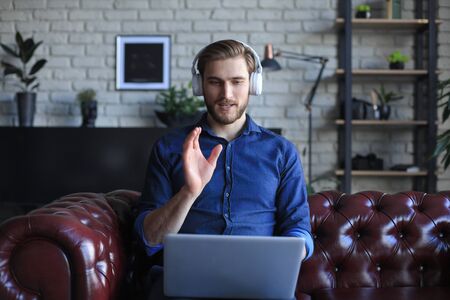 Concentrated young freelancer businessman sitting on sofa with laptop, working remotely online at...