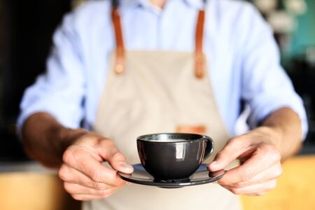 Barista offering a cup of coffee to camera at the coffee shopの写真素材