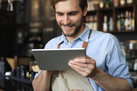 Young male owner using digital tablet while standing in cafeの写真素材