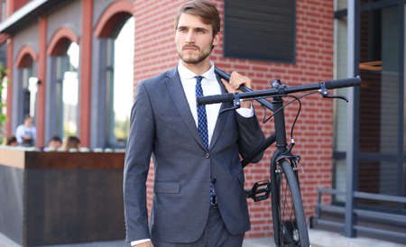 Handsome young businessman carrying his bicycle on shoulder while walking outdoors