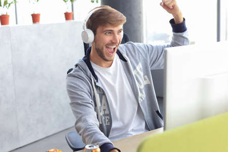 Portrait of ecstatic gamer guy in headphones screaming and rejoicing while playing video games on computerの写真素材