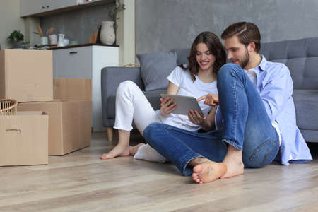 Happy couple sitting and planning new home decoration at home with a tablet at moving day,...