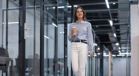 Businesswoman walking along the office corridor with paper cup