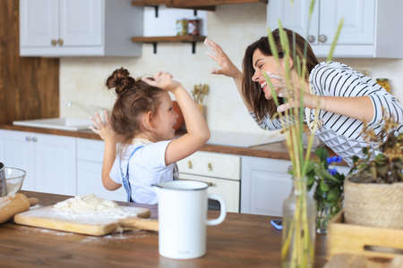 Playful little girl cooking at kitchen with her loving motherの写真素材