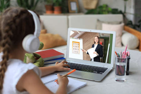 Distance learning. Cheerful little girl girl in headphones using laptop studying through online e-learning systemの写真素材